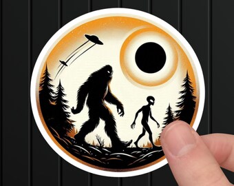 May include: A round sticker with a black silhouette of Bigfoot and an alien walking side-by-side in front of a glowing orange sun with a black hole in the center. Two flying saucers are in the sky above.