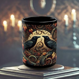 May include: Black ceramic mug with a design of two black ravens perched on branches with a moon and swirling vines in the background. The design is in shades of brown, orange, and green.