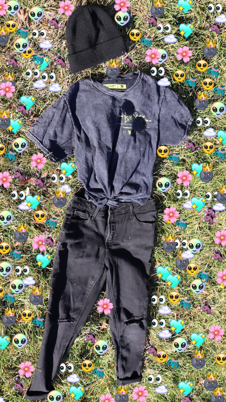 Pode incluir: Um gorro preto, uma camiseta cinza escura com o texto "The Bahamas" e um gr&aacute;fico, e cal&ccedil;as jeans pretas com joelhos desgastados s&atilde;o colocados em uma cama de grama verde com adesivos de emoji coloridos.