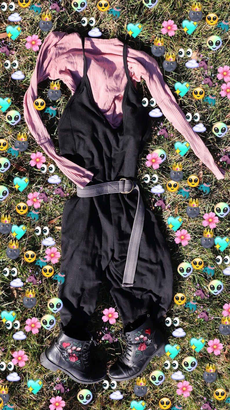 Pode incluir: Um macac&atilde;o preto com uma camisa rosa de manga comprida sobreposta. O macac&atilde;o tem um cinto largo cinza e a camisa tem uma textura canelada. O conjunto est&aacute; colocado sobre um leito de grama verde com gr&aacute;ficos de desenhos animados coloridos.