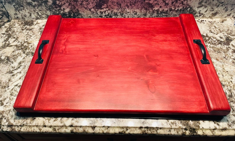 May include: A large, rectangular wooden serving tray with two black metal handles on each side. The tray is stained a deep red colour.