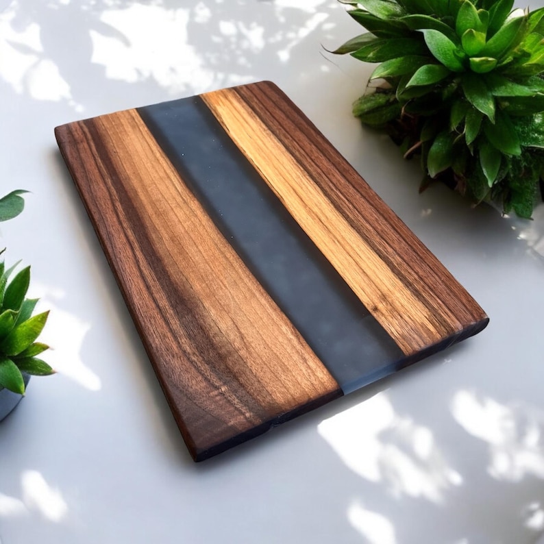 K&ouml;nnte beinhalten: Ein rechteckiges Schneidebrett aus Holz mit einer Einlage aus dunkelgrauem Epoxidharz. Das Brett hat eine nat&uuml;rliche Holzmaserung und ist perfekt zum Servieren von K&auml;se, Wurstwaren oder anderen Vorspeisen.