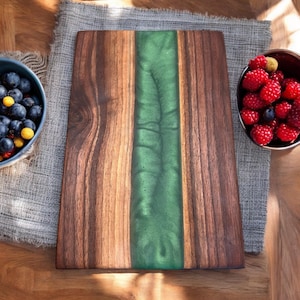 K&ouml;nnte beinhalten: Ein rechteckiges Schneidebrett aus Holz mit einem gr&uuml;nen Epoxidharzeinleger. Das Brett hat eine nat&uuml;rliche Holzmaserung und ist perfekt zum Servieren von K&auml;se, Wurstwaren oder anderen Vorspeisen.