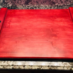 May include: A large, rectangular wooden serving tray with two black metal handles on each side. The tray is stained a deep red color.