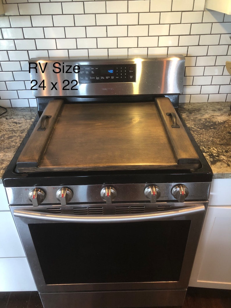 May include: A stainless steel stovetop with a wooden cutting board on top. The stovetop has four burners and an oven. The cutting board is 24 inches by 22 inches. The stovetop is labeled "Samsung".