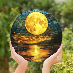 May include: A stained glass window depicting a full moon over a lake at sunset. The moon is yellow and the lake is blue with a reflection of the moon. The sky is a gradient of orange, yellow, and blue.