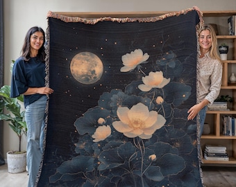 May include: A woven throw blanket with a dark blue background featuring a large moon and white flowers with gold accents. The flowers are stylized and have a soft, dreamy look. The moon is full and has a soft glow. The blanket has a fringed edge.