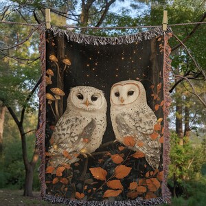 Cotton woven throw blanket displaying snowy owl pair in mystical nighttime forest scene with autumn foliage, mushrooms and twinkling stars