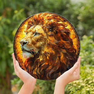 May include: A stained glass artwork depicting a lion's head in profile. The lion is rendered in shades of gold, amber, and brown, with intricate details in the mane and fur.