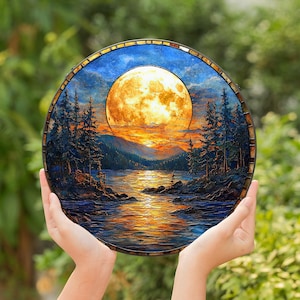May include: A round, stained glass art piece depicting a moonlit lake scene. The artwork features a large, glowing moon, a body of water, and silhouetted trees. The color palette includes blues, oranges, and yellows, creating a serene and naturalistic landscape.