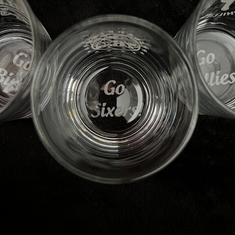 May include: Three clear glass tumblers with the words "Go Sixers!" etched on the bottom. The glasses are stacked on top of each other.