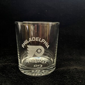 May include: A clear glass tumbler with the Philadelphia Flyers logo and the words "Philadelphia Flyers Go" etched into the glass.