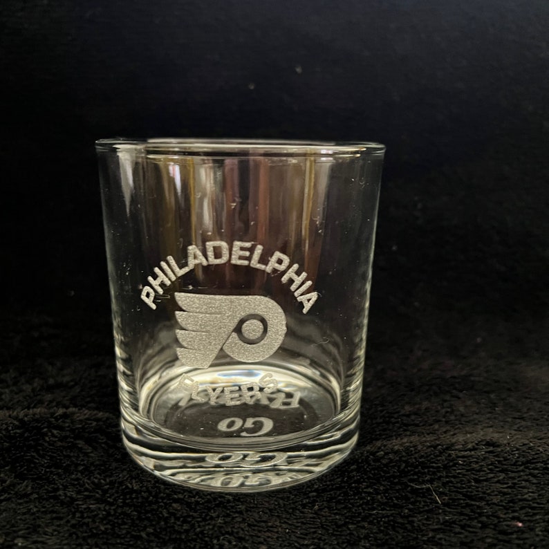 May include: A clear glass tumbler with the Philadelphia Flyers logo and the words "Philadelphia Flyers Go" etched into the glass.