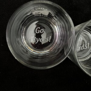 May include: Two clear glass tumblers with the words "Go Flyers!" etched into the bottom. The glasses are on a black surface.