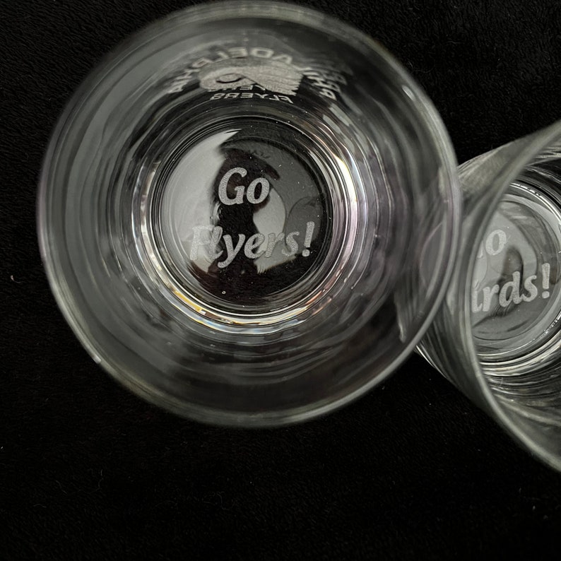 May include: Two clear glass tumblers with the words "Go Flyers!" etched into the bottom. The glasses are on a black surface.