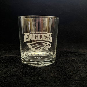 May include: A clear glass tumbler with an etched design of the Philadelphia Eagles logo and the words "Philadelphia Eagles" and "Go Birds".