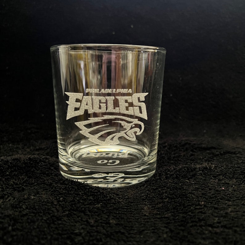 May include: A clear glass tumbler with an etched design of the Philadelphia Eagles logo and the words "Philadelphia Eagles" and "Go Birds".