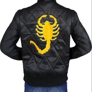 K&ouml;nnte beinhalten: Schwarze, gesteppte Bomberjacke mit gelbem Skorpion-Emblem auf dem R&uuml;cken. Die Jacke hat einen gerippten Kragen und B&uuml;ndchen. Das Skorpion-Design ist detailliert und mittig auf dem R&uuml;cken der Jacke platziert.