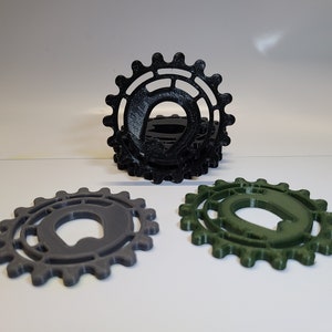 May include: Three 3D printed gears, one black, one gray, and one green. Each gear has a unique design with a hole in the center.