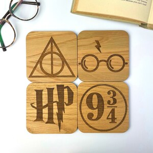 May include: Set of four wooden coasters featuring Harry Potter themed designs. The coasters feature the Deathly Hallows symbol, a pair of glasses with a lightning bolt, the Harry Potter logo, and the Platform 9 3/4 sign.