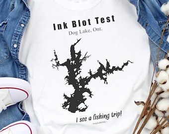 Può includere: Maglietta bianca con un design a macchia d'inchiostro nero del lago Dog, Ontario. Il testo "Ink Blot Test" e "Dog Lake, Ont." è stampato sopra il design. Il testo "I see a fishing trip!" è stampato sotto il design.
