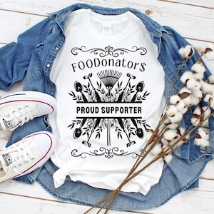 White and black vegetable shirt saying FOODonator$ proud supporter.