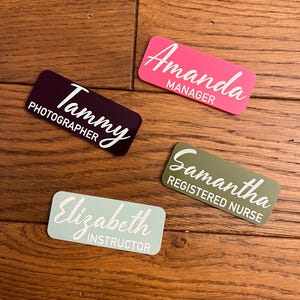 Peut inclure: Quatre badges nominatifs rectangulaires de différentes couleurs : prune, rose, vert sauge et bleu clair. Chaque badge comporte un nom en écriture cursive et un titre en sans-serif. Les noms sont Tammy, Amanda, Samantha et Elizabeth.