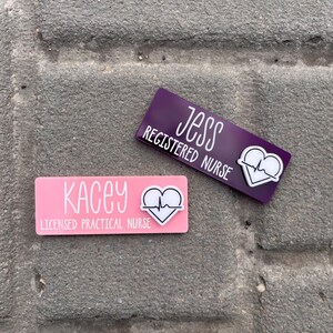 May include: Two pink and purple name tags with a heart beat symbol and the text "Kacey Licensed Practical Nurse" and "Jess Registered Nurse".