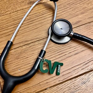 May include: A black stethoscope with a silver tube and a green keychain with the letters "CV" and the name "Jenna" on it.