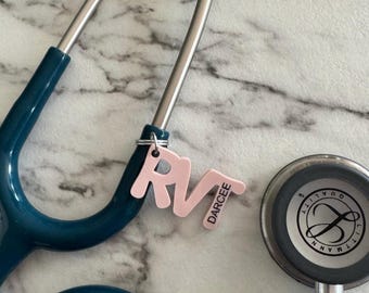 Puede incluir: Un estetoscopio azul turquesa con un dije de letras rosa que dice "RV" y "DARCEE".
