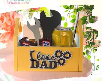 Pode incluir: Uma caixa de ferramentas de madeira amarela com as palavras "I love DAD" na frente. A caixa de ferramentas contém uma lata de cerveja, duas barras de chocolate, uma chave inglesa e uma chave de fenda.