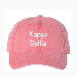 May include: A coral baseball cap featuring the embroidered text "Kappa Delta" in white. The cap has a curved peak and a classic six-panel design, suitable for casual wear.