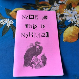 May include: A pink zine with the text "None of This is Normal" in a bold, cut-out style font. The cover features a black and white illustration of two vultures. The zine is on a blue floral patterned surface.