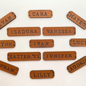 Custom leather name tags with various names displayed on a light background.
