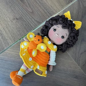Handmade crocheted amigurumi doll named Orange Girl, featuring a personalized leather name label and accompanied by a marmalade-colored butterfly pet. Perfect gift for children and collectors.