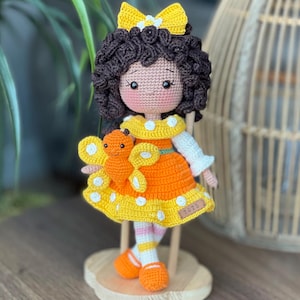 Handmade crocheted amigurumi doll named Orange Girl, featuring a personalized leather name label and accompanied by a marmalade-colored butterfly pet. Perfect gift for children and collectors.