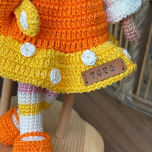 Handmade crocheted amigurumi doll named Orange Girl, featuring a personalized leather name label and accompanied by a marmalade-colored butterfly pet. Perfect gift for children and collectors.