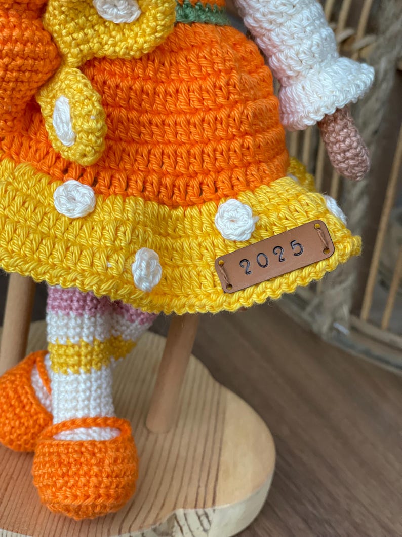 Handmade crocheted amigurumi doll named Orange Girl, featuring a personalized leather name label and accompanied by a marmalade-colored butterfly pet. Perfect gift for children and collectors.