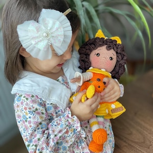 Handmade crocheted amigurumi doll named Orange Girl, featuring a personalized leather name label and accompanied by a marmalade-colored butterfly pet. Perfect gift for children and collectors.