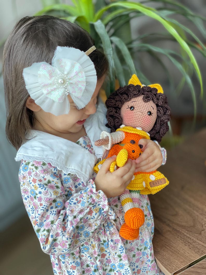 Handmade crocheted amigurumi doll named Orange Girl, featuring a personalized leather name label and accompanied by a marmalade-colored butterfly pet. Perfect gift for children and collectors.