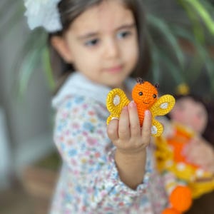 Handmade crocheted amigurumi doll named Orange Girl, featuring a personalized leather name label and accompanied by a marmalade-colored butterfly pet. Perfect gift for children and collectors.