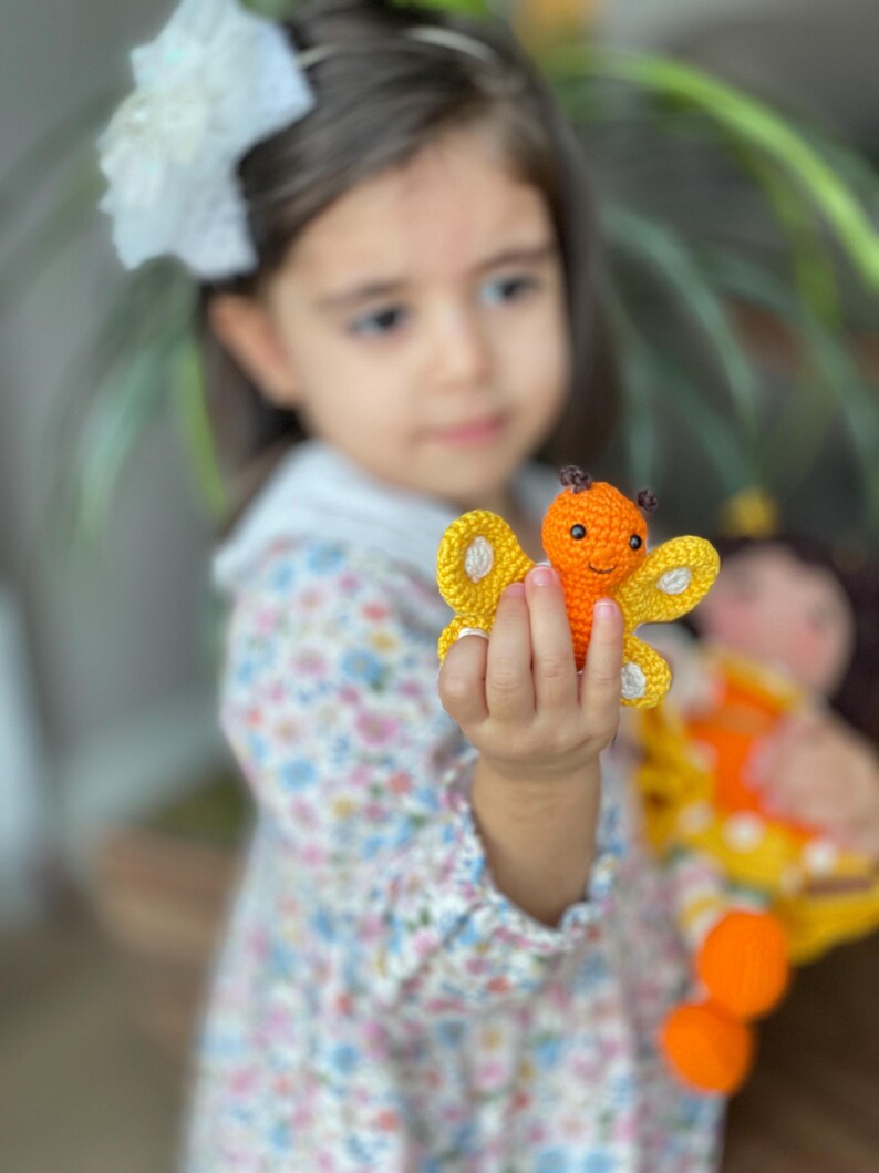Handmade crocheted amigurumi doll named Orange Girl, featuring a personalized leather name label and accompanied by a marmalade-colored butterfly pet. Perfect gift for children and collectors.