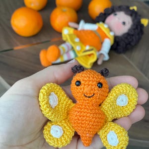 Handmade crocheted amigurumi doll named Orange Girl, featuring a personalized leather name label and accompanied by a marmalade-colored butterfly pet. Perfect gift for children and collectors.