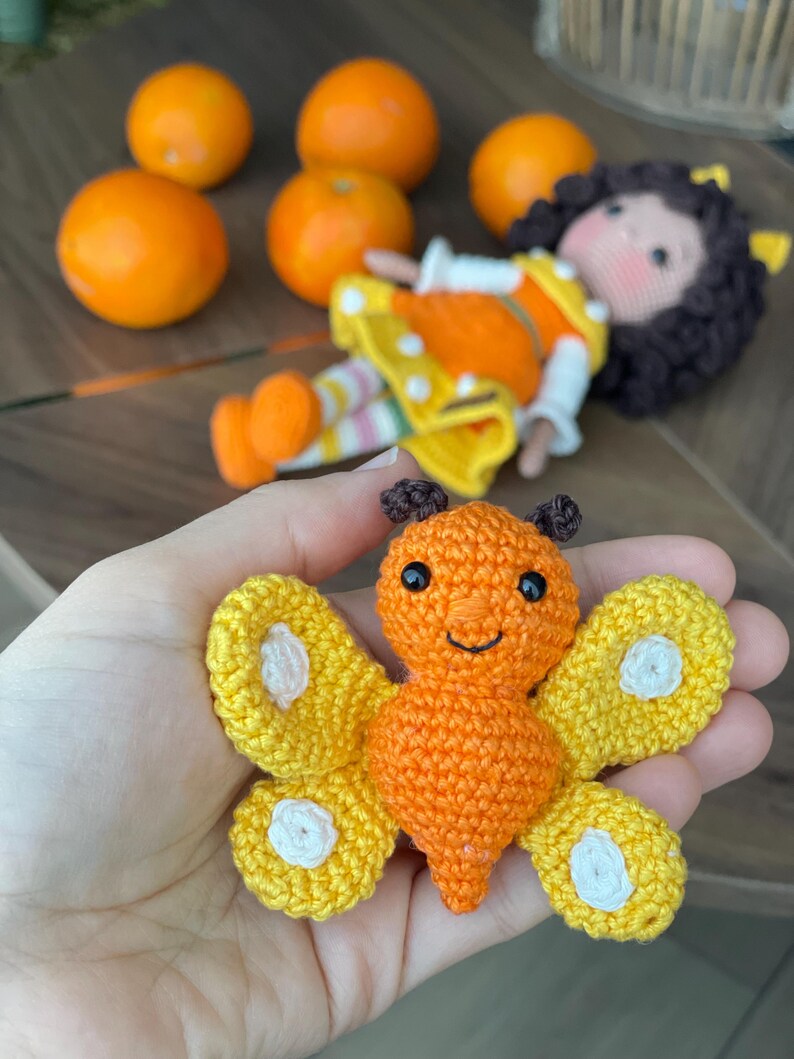 Handmade crocheted amigurumi doll named Orange Girl, featuring a personalized leather name label and accompanied by a marmalade-colored butterfly pet. Perfect gift for children and collectors.