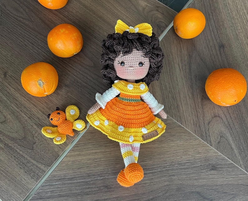 Handmade crocheted amigurumi doll named Orange Girl, featuring a personalized leather name label and accompanied by a marmalade-colored butterfly pet. Perfect gift for children and collectors.