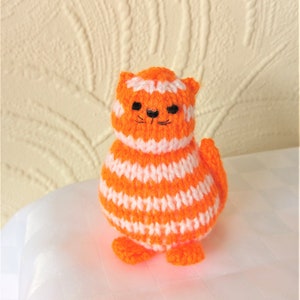 May include: A small, orange and white striped knitted cat toy. The cat has black eyes and a black nose.