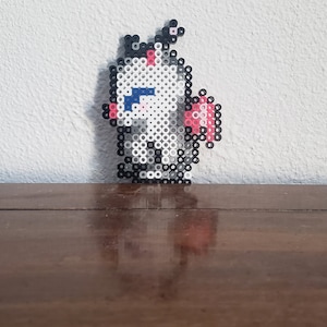 Puede incluir: Un unicornio de pixel art blanco y rosa con ojos azules, de pie sobre una superficie de madera.