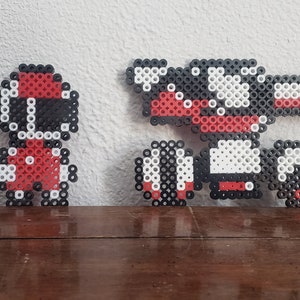 Könnte beinhalten: Eine rote und weiße Pixel-Art-Figur eines Charakters mit Helm, die neben einer größeren roten, weißen und schwarzen Pixel-Art-Figur eines Roboters mit einer Waffe steht.