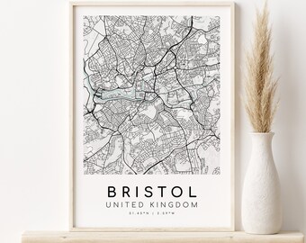 May include: A black and white map print of Bristol, United Kingdom, in a white frame on a wooden shelf. The map shows the city's streets and waterways. The text "BRISTOL" and "UNITED KINGDOM" is printed below the map, along with the coordinates "51.45°N | 2.59°W".