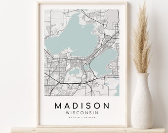 May include: A framed print of a map of Madison, Wisconsin. The map is in black and white with a light blue color for the lakes. The text below the map reads "MADISON WISCONSIN 43.07°N | 89.40°W".